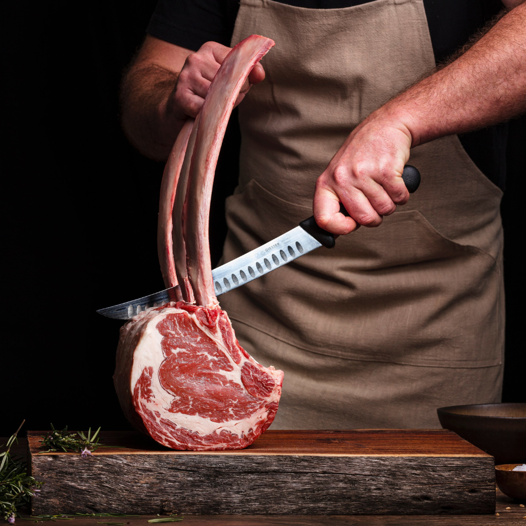 chef cutting a tomahawk steak in an apron
